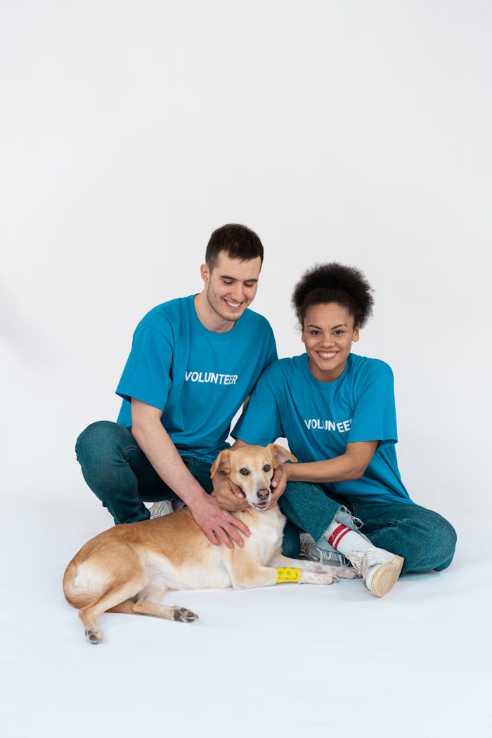 A happy couple of volunteers smiling while posing with a rescue dog in a studio setting.